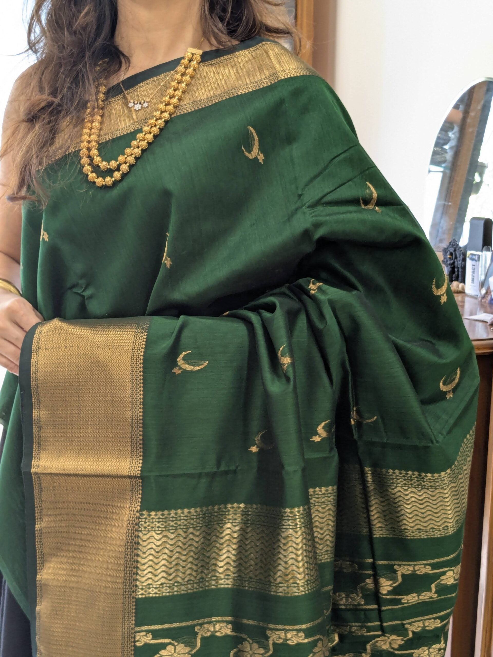 Close-up of bottle green Maheshwari saree with moon and flower motifs, wide-narrow border