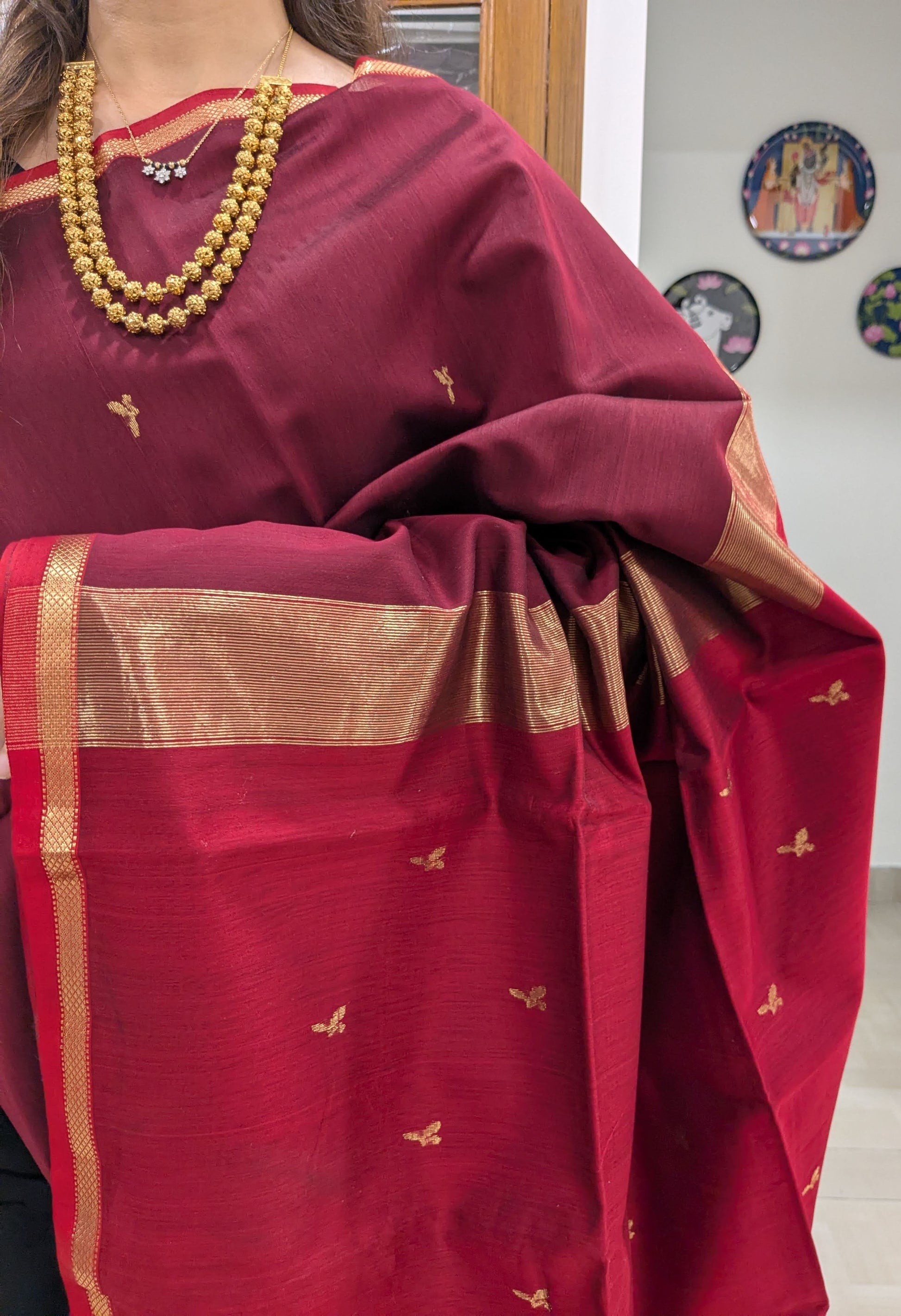 Close-up of maroon Maheshwari saree with leaf butti motifs, handloom weave, and small border detailing.