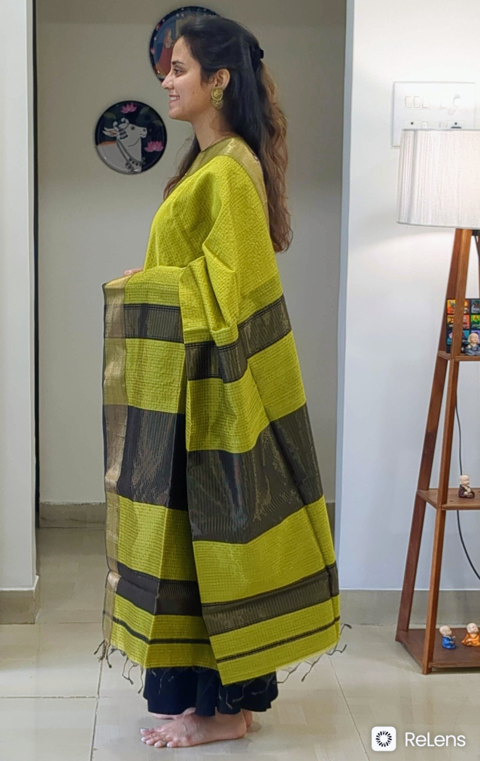 Side view of mehendi green saree showcasing rich drape, intricate weave, and shimmering zari detail.