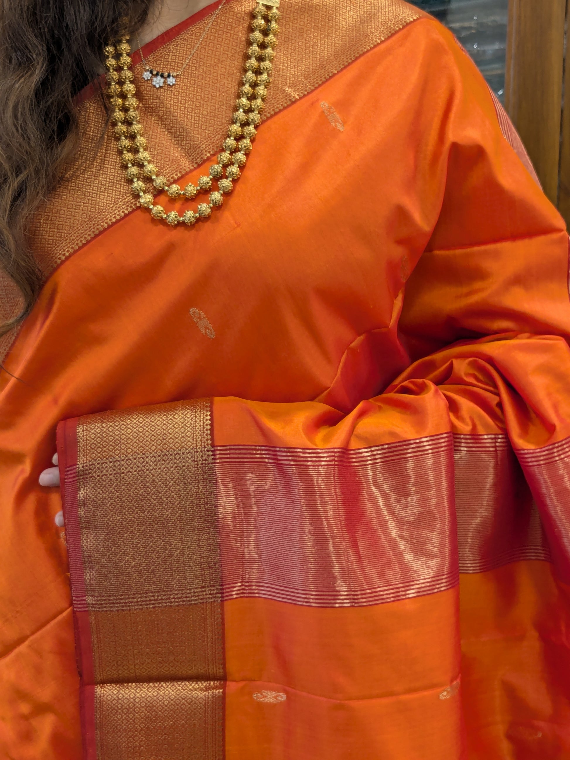 Close-up of Sunset Orange pure silk Maheshwari saree with intricate butti, jaali border, and butticar pallu.