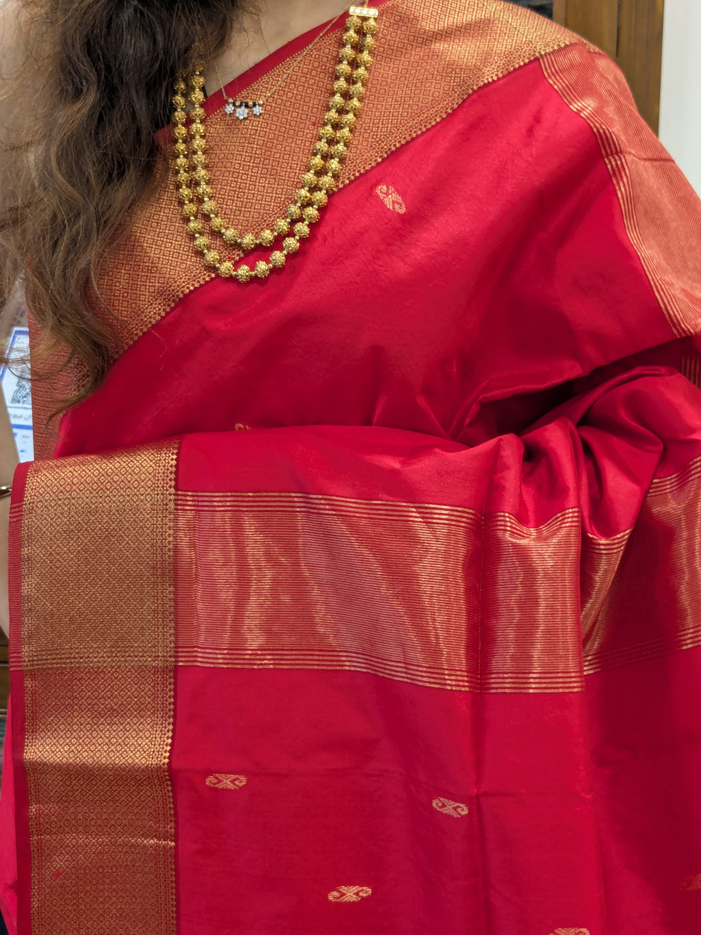 Close-up of Tomato Red pure silk Maheshwari saree with intricate butti and ornate jaali border.