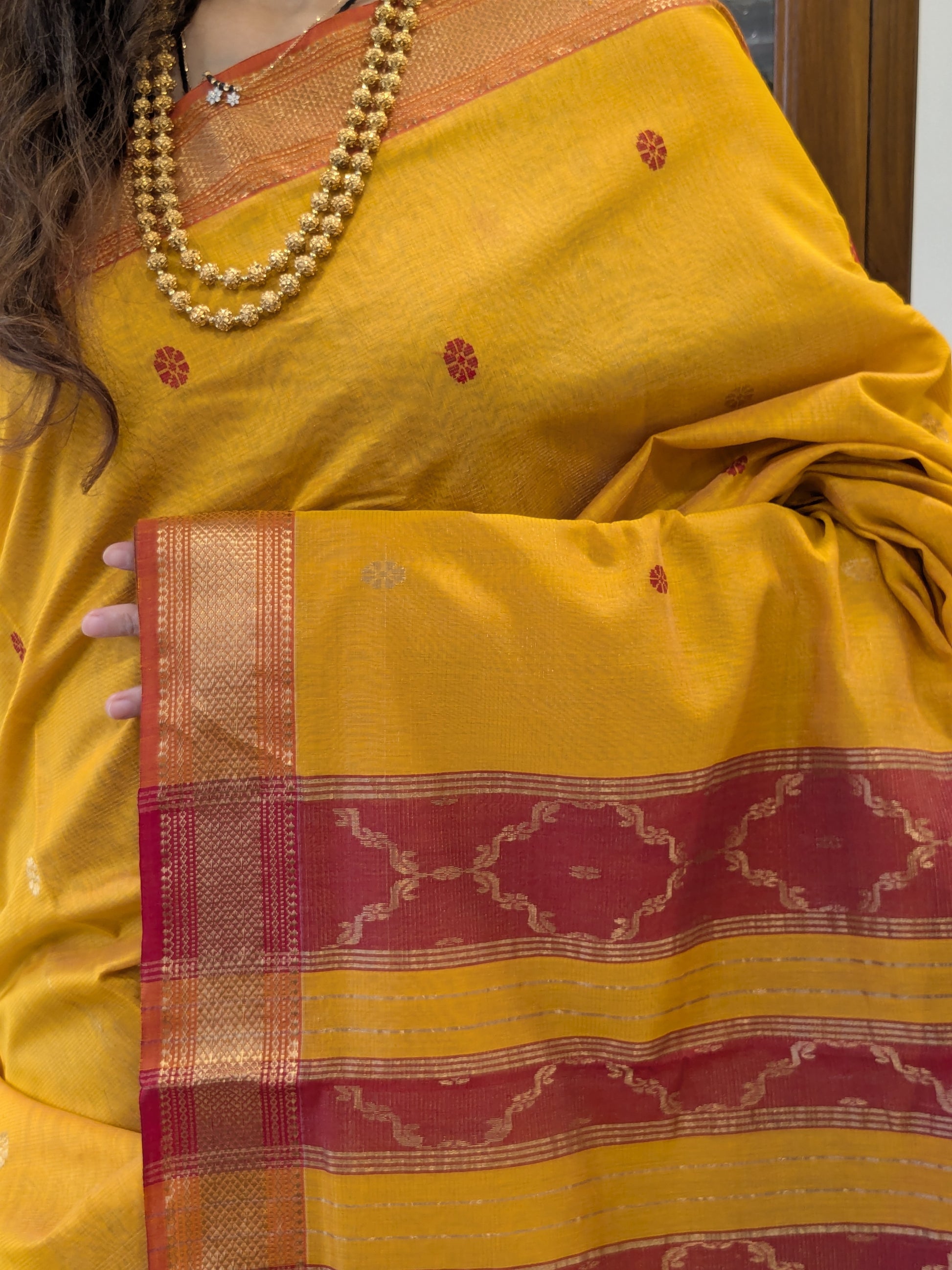 Close-up of yellow silk tissue Maheshwari saree with flower butti, jaali pallu, and small border.