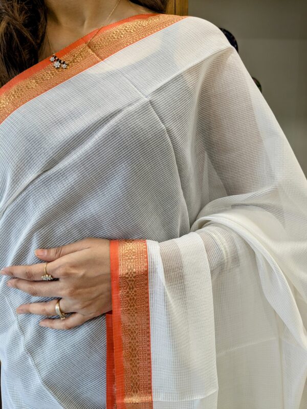 Close-up of white Maheshwari saree with small checks, handwoven texture, zari border, and vintage pallu transition.