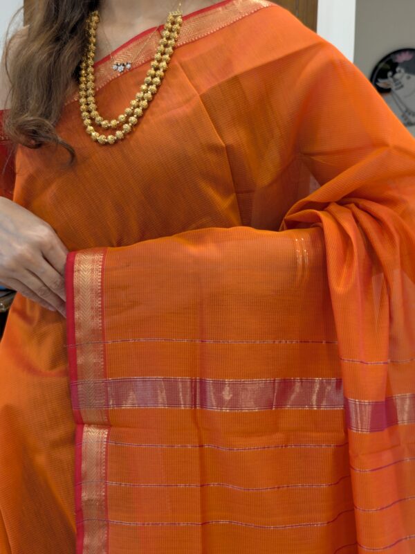 Close-up of rust orange Maheshwari silk-cotton saree with striped design, small zari border